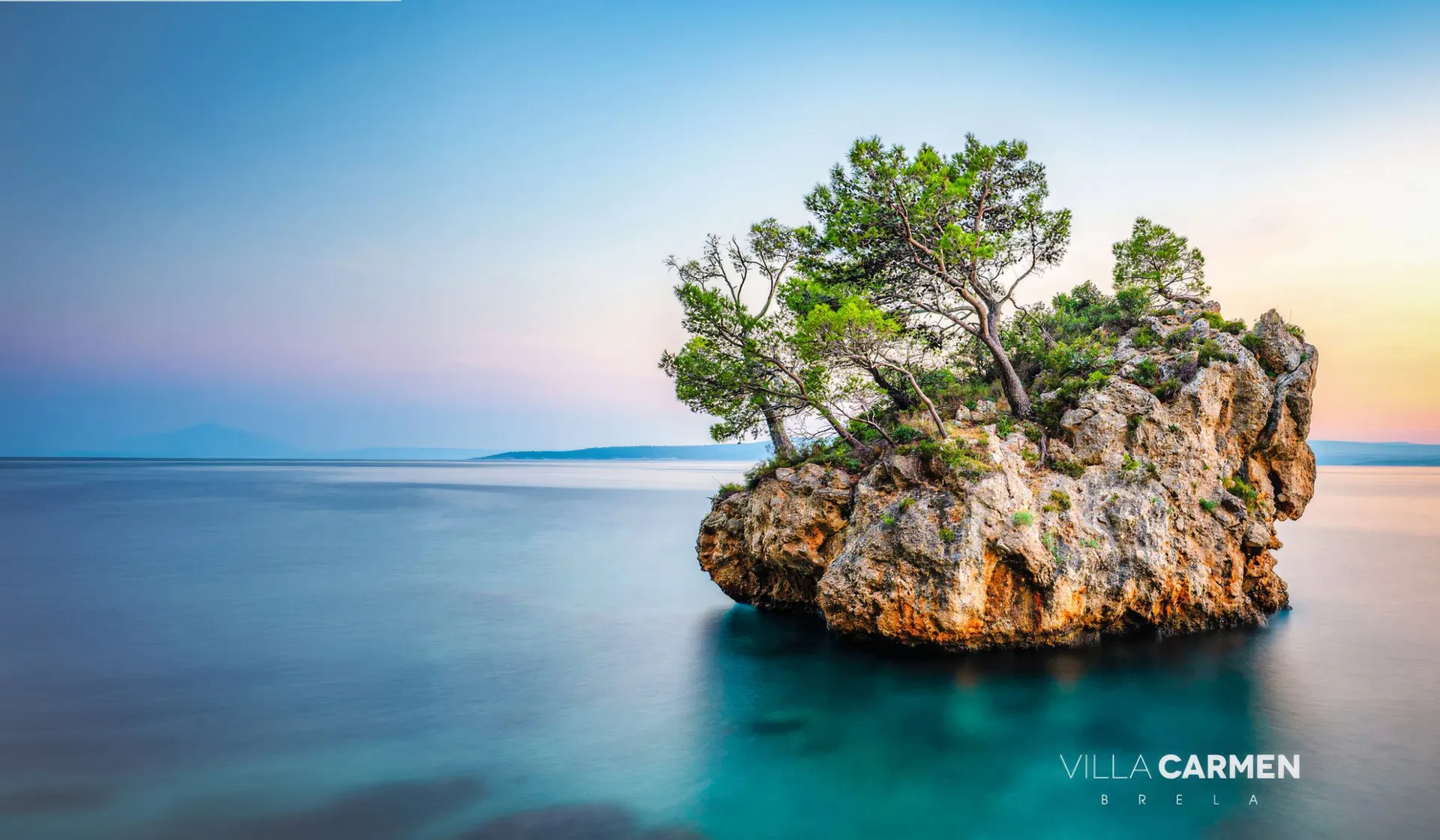Kamen Brela, the rock islet with pine trees in calm turquoise sea, Brela